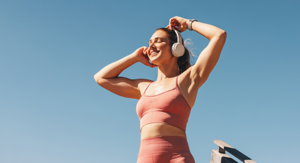 Woman in athletic wear standing listening to wellness music on headphones outside