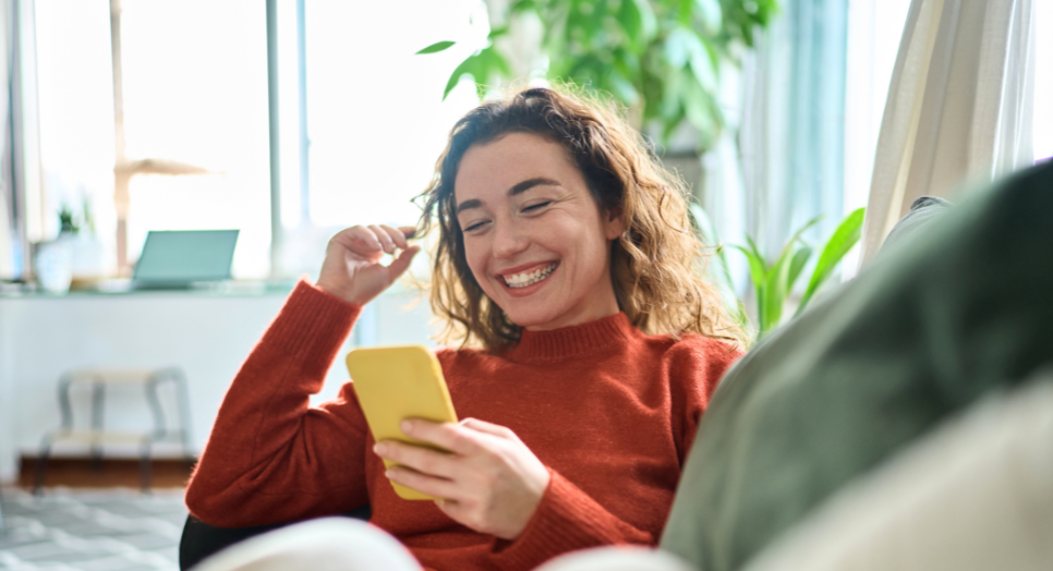 Woman at home holding smart phone amused by social media app