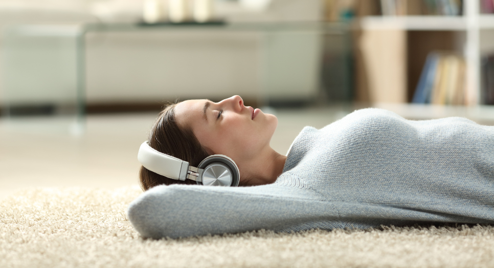 woman wearing winter sweater lying on rug listening to music on headphones 